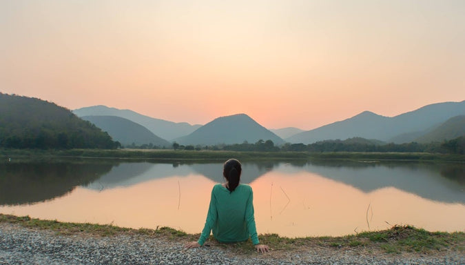 woman sitting near edge of lake during sunset