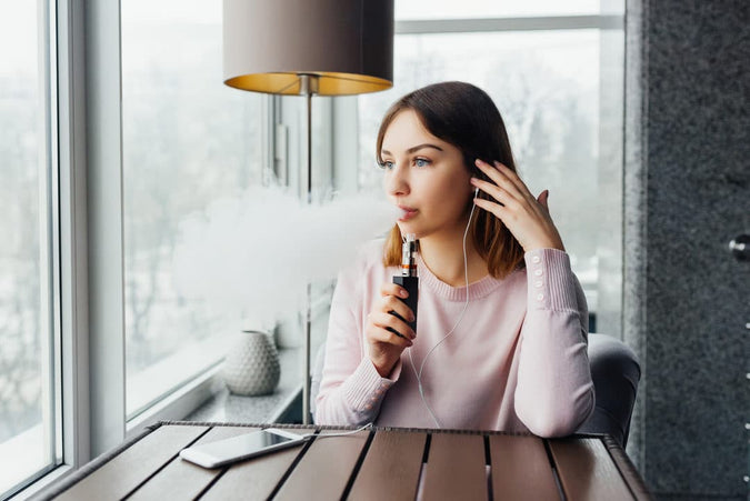 Woman vaping and sitting at a table