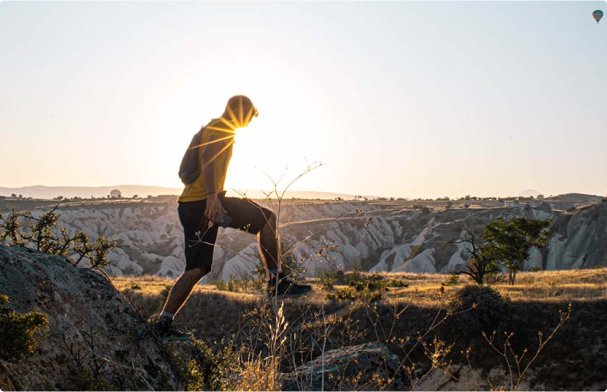 Man walking over a mountain plateu with the sun lense flare directly infront of his body