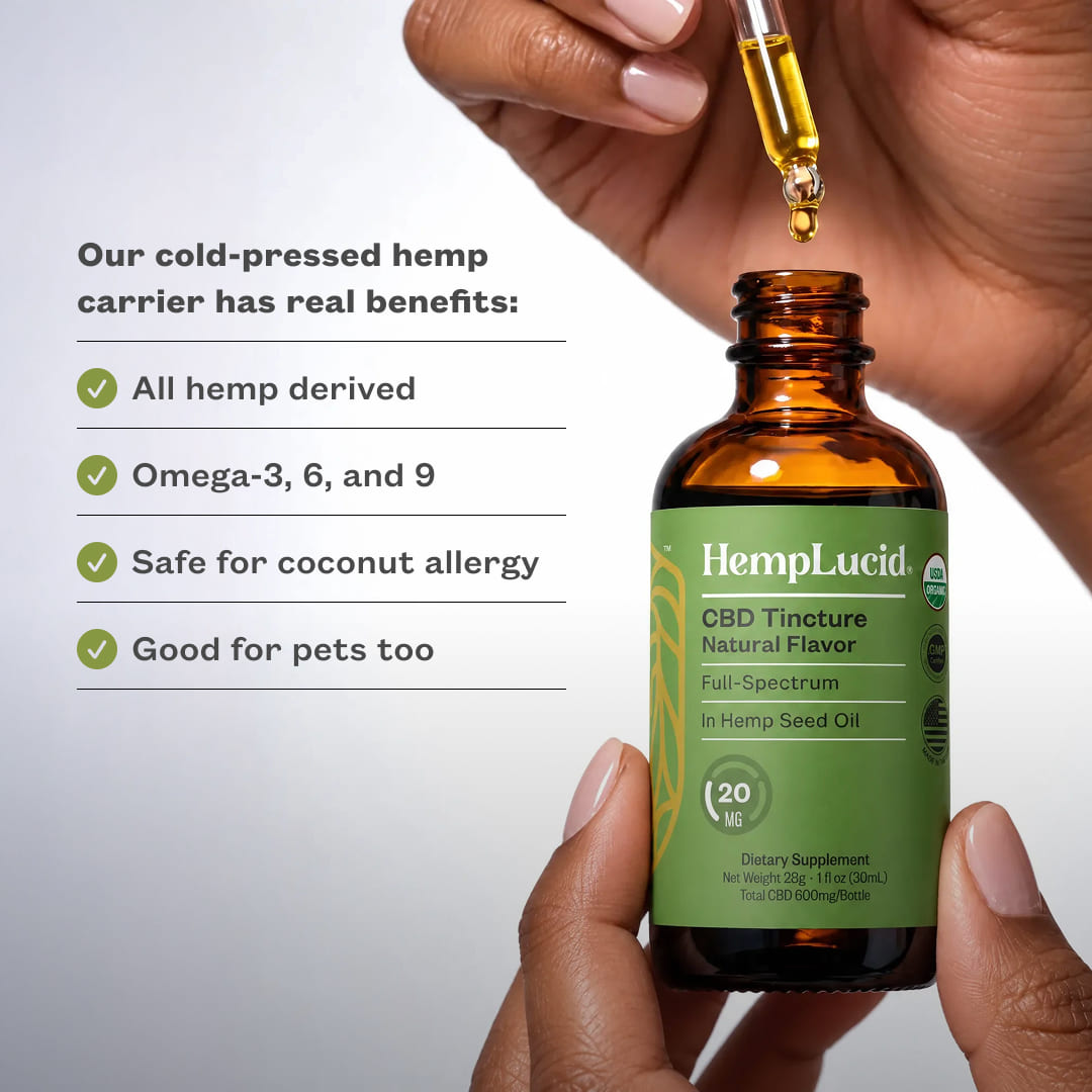 A person holds an amber glass bottle of HempLucid CBD Tincture Natural Flavor with a green label, while another hand holds a glass dropper above the bottle. Text on the left reads. "Our cold-pressed carrier has real benefits: All hemp derived, Omega-3, 6, and 9, Safe for coconut allergy, Good for pets too.