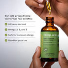 A person holds an amber glass bottle of HempLucid CBD Tincture Natural Flavor with a green label, while another hand holds a glass dropper above the bottle. Text on the left reads. "Our cold-pressed carrier has real benefits: All hemp derived, Omega-3, 6, and 9, Safe for coconut allergy, Good for pets too.