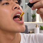 A close-up of a man applying a HempLucid Full-spectrum CBD Tincture in Hemp Seed Oil from a liquid dropper under his tongue in a bathroom setting.